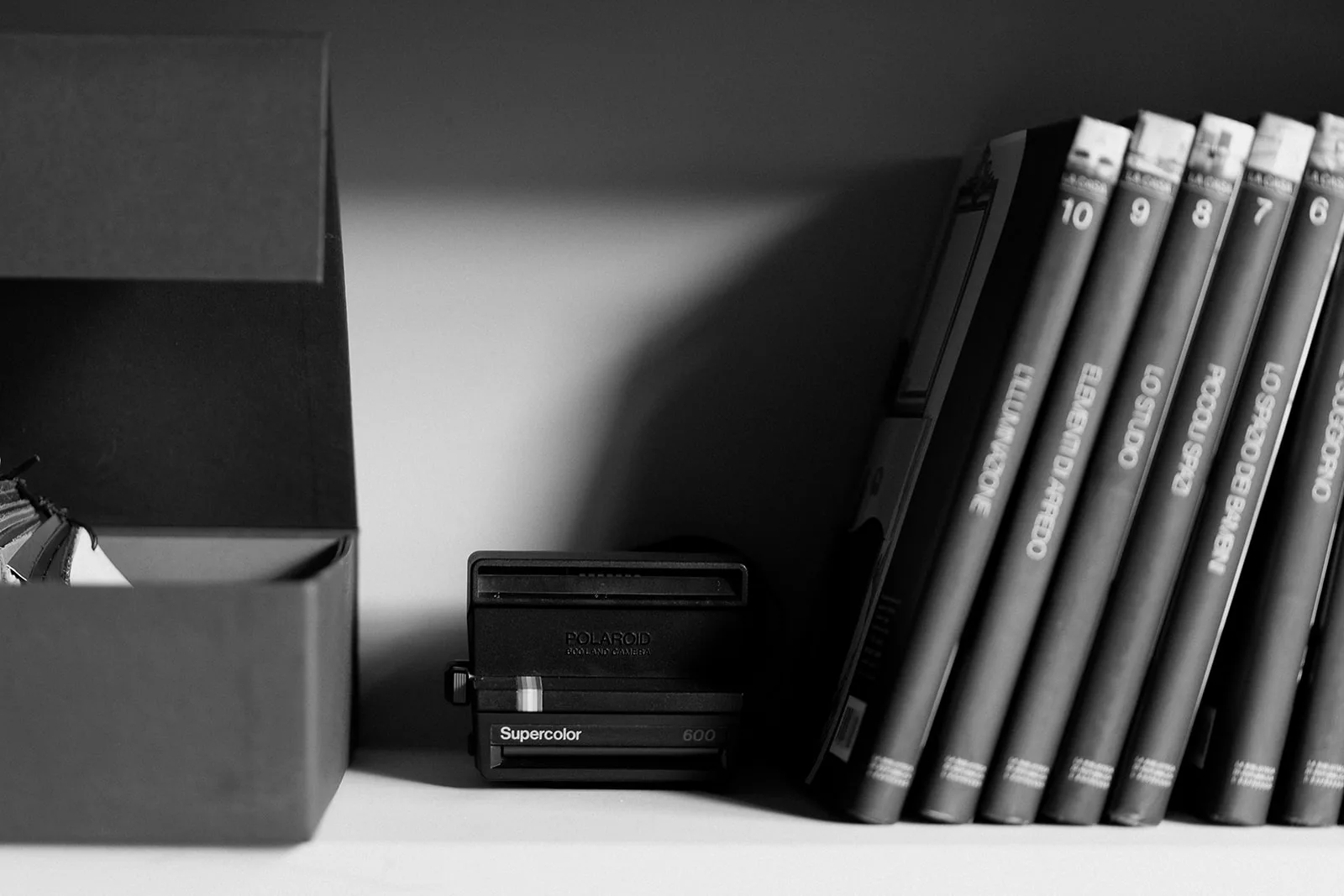 Fotocamera Polaroid vintage e libri di design su una mensola